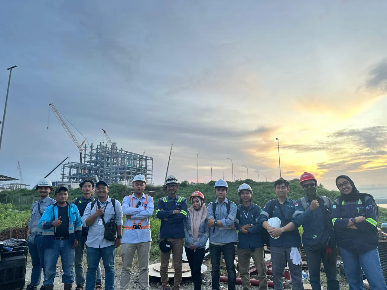 Tim instalasi E&I PT TEM di lokasi proyek kilang dengan latar struktur plant dan tower crane
